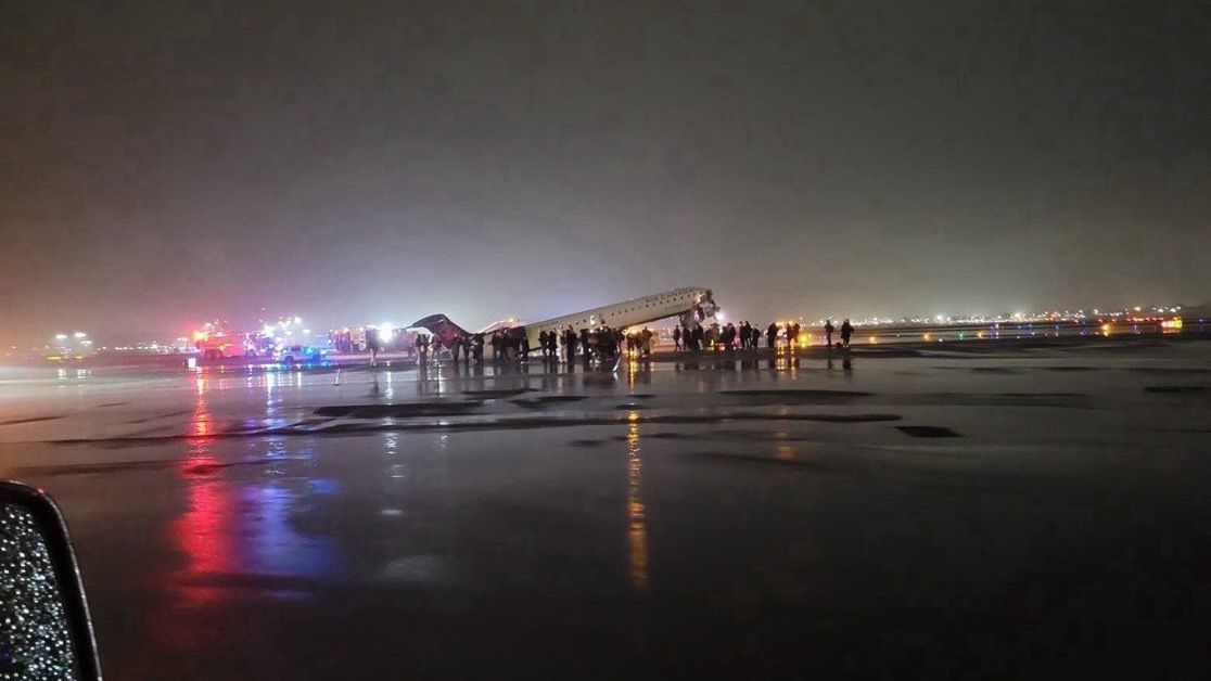 Wide view of the LaGuardia crash scene, Air Canada Express CRJ-900 tilted with nose destroyed on Runway 4, emergency vehicles surrounding the aircraft