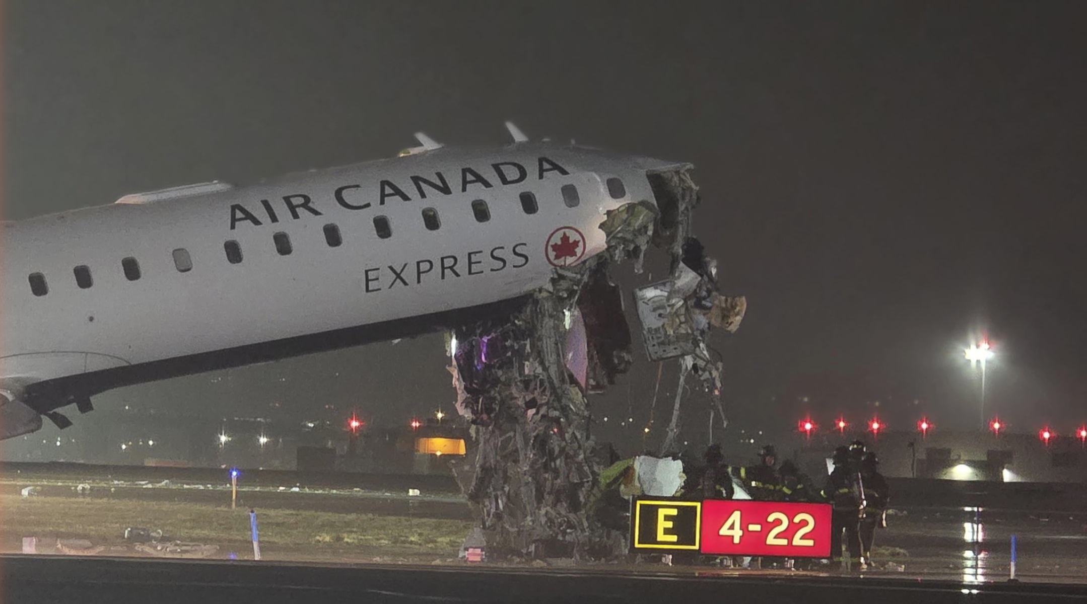 Air Canada Express CRJ-900 nose completely destroyed after striking a Port Authority fire truck on Runway 4 at LaGuardia Airport: Exit E, Runway 4-22 sign visible in foreground