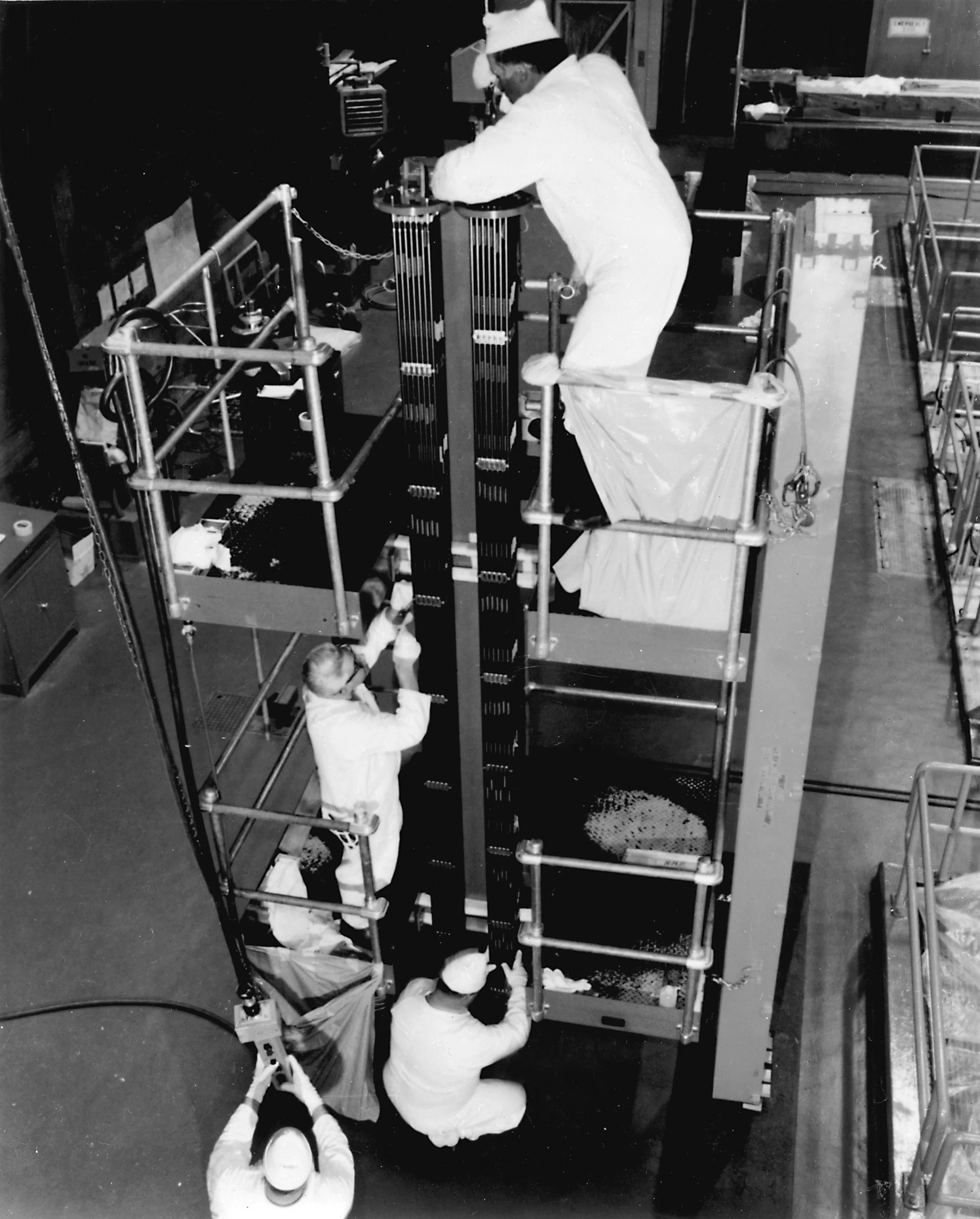 Workers in white coveralls handling a nuclear fuel assembly at Nine Mile Point Unit 1 around 1969