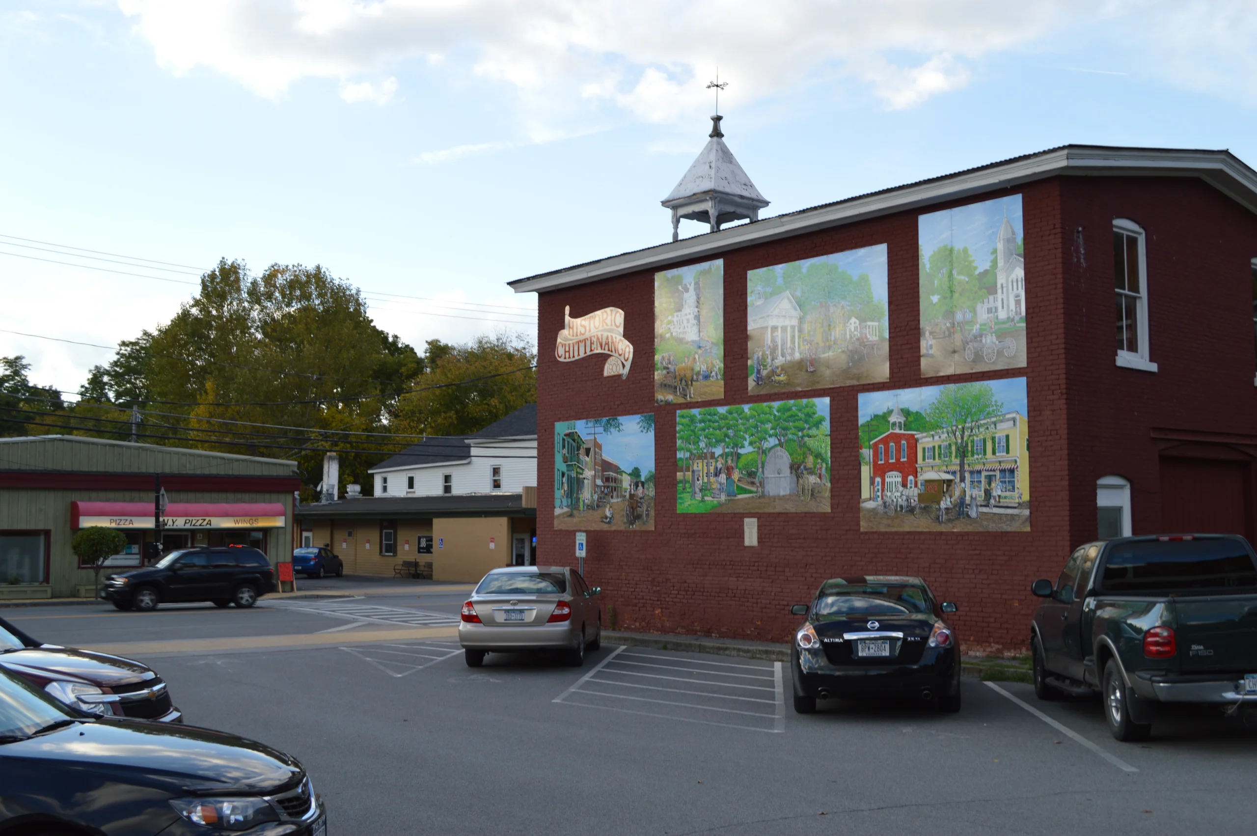 Murals of historic village scenes on the brick wall of a downtown Chittenango building beside a parking lot