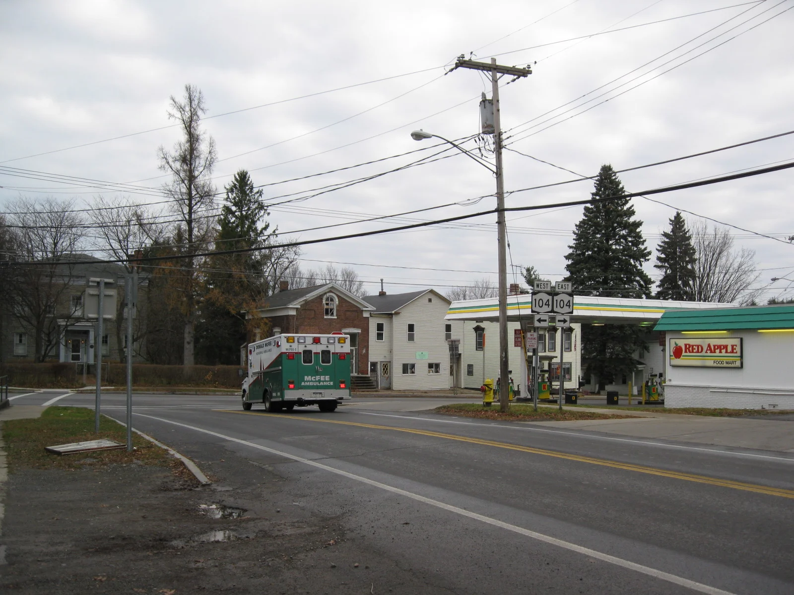 A street corner in Mexico New York with Route 104 signs, a food mart and an ambulance passing