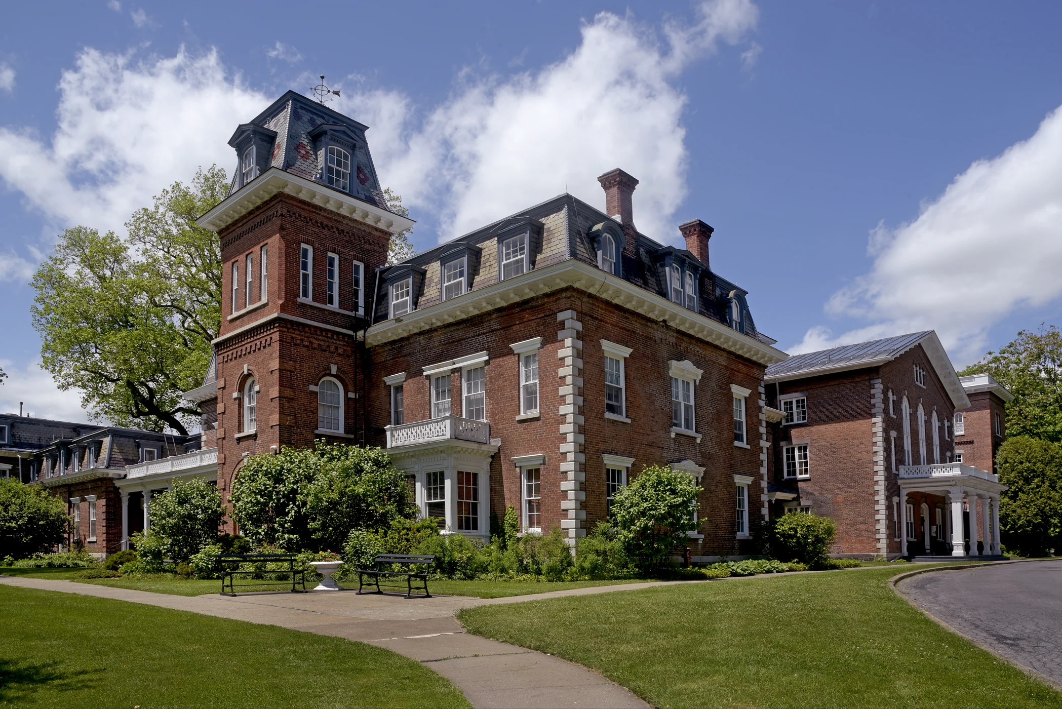 The large brick Oneida Community Mansion House with its tower and mansard roof under a blue sky