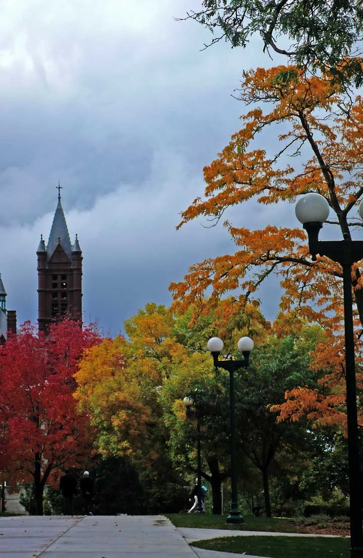Orange and red autumn foliage on the Syracuse University campus with a Gothic stone tower behind